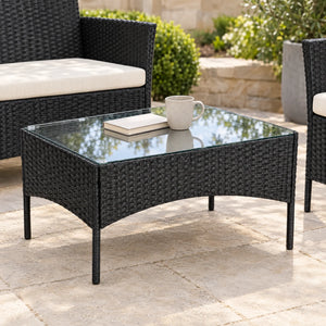Glass-top black rattan coffee table styled with a mug and books on a garden patio