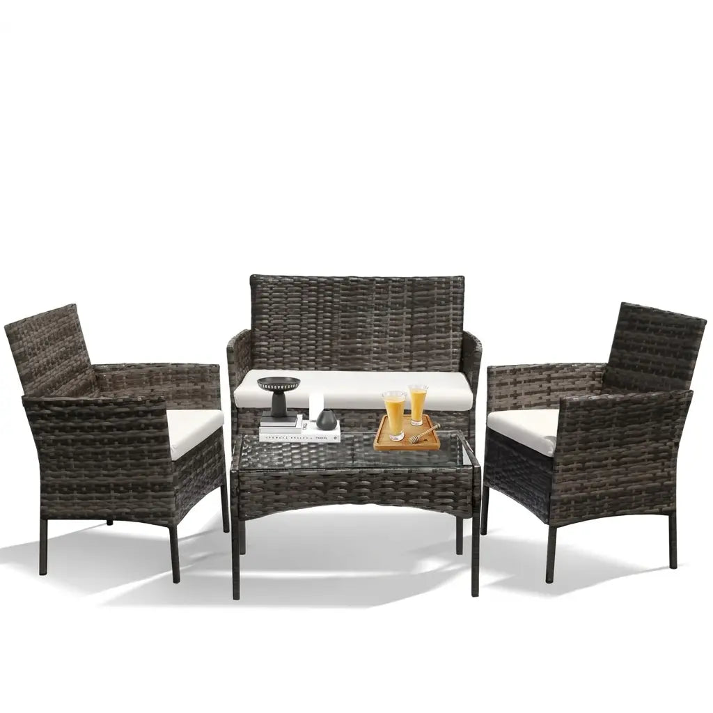 Grey rattan 4-piece patio furniture set with a loveseat, two armchairs, white cushions and a glass-top coffee table.