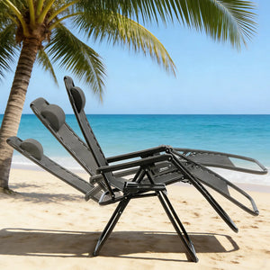 Two black zero-gravity reclining chairs shown in a fully reclined position on a tropical beach