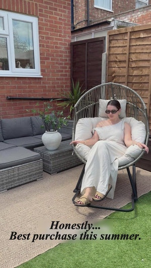 Woman demonstrating the Oversized Egg Rattan Rocking Chair in a modern British garden, showing its spacious seat and smooth rocking motion.